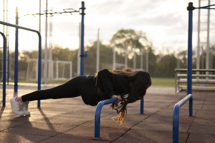 Vrouw traint haar bovenlichaam met incline push-ups op een buitensportplek bij zonsondergang