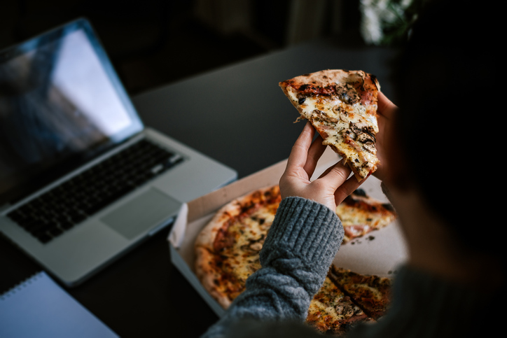 Persoon eet pizza en zit achter laptop