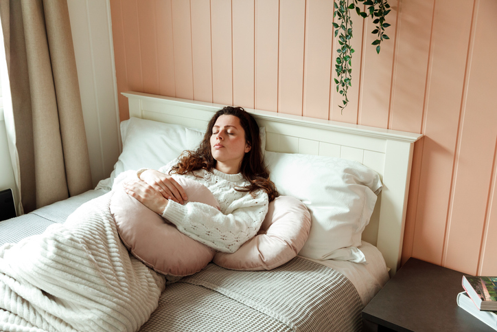 Jonge vrouw ligt met menstruatieklachten op bed.