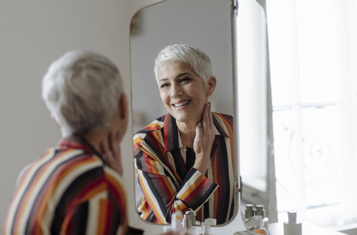 Vrouw op leeftijd lacht naar zichzelf in spiegel