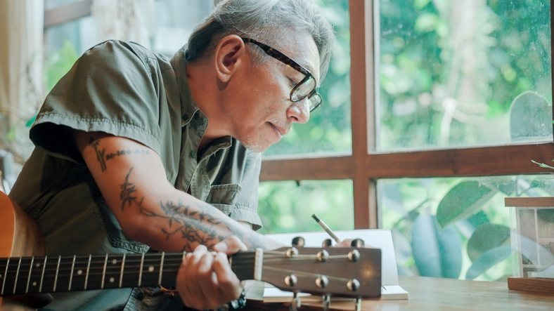 Man met gitaar in hand schrijft iets op