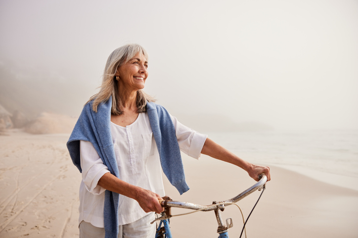 Vrouw op leeftijd bij het strand met een fiets in de hand
