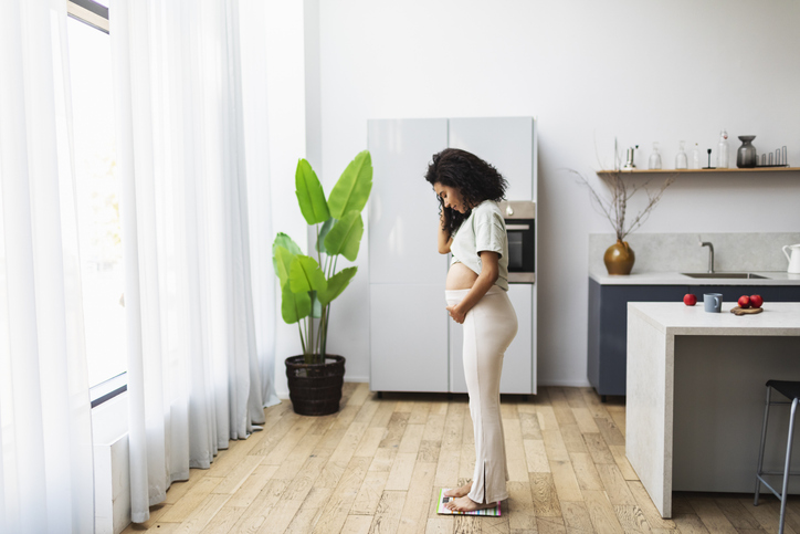 Zwangere vrouw weegt zichzelf op weegschaal in de keuken.