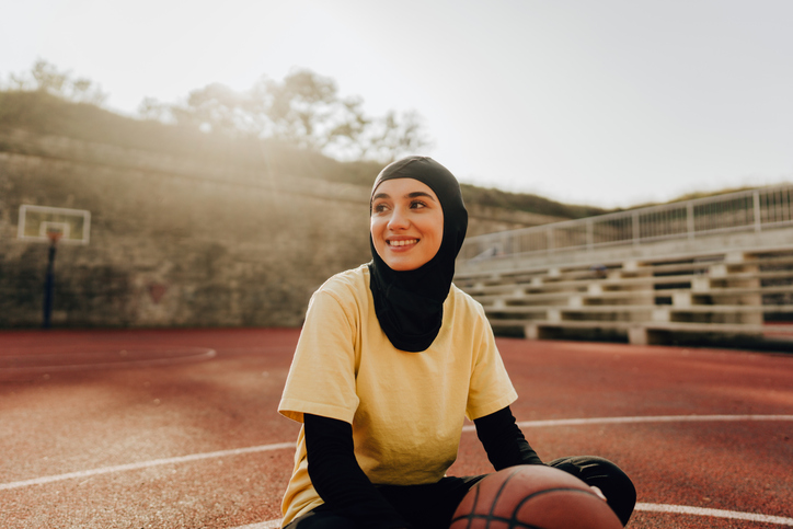 Gesluierde vrouw zit op basketbal veld met een basketbal